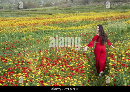 Attraktive junge Frau in rotem Kleid, die glücklich im Frühlingsfeld mit Mohnblumen läuft. Frühlingszeit Zypern Stockfoto