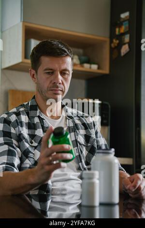 Der Mann sitzt am Tisch in der Küche und sieht sich verschiedene Flaschen mit Medikamenten-Kapseln an. Die Person nimmt Pillen oder Vitamine ein. Das Konzept der Nahrungsergänzungsmittel, medici Stockfoto