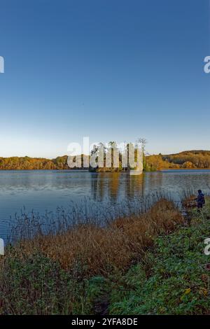 Ein einsamer Fischer am Ufer des Loch of Clunie, mit Clunie Castle und Insel im Hintergrund unter tiefblauem Himmel. Stockfoto