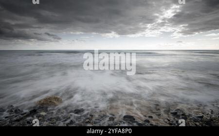 Meereswellen plätschern vor stürmischem, dramatisch bewölktem Himmel an die Küste mit Kieselsteinen. Winterzeit, Langlebigkeit Limassol zypern Stockfoto