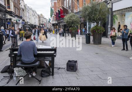 Dublin, Irland, Juli 21 2022: Junger pianistischer Straßenmusiker spielt Klavier in der grafton Sopping Street in Dublin, irland, mit Leuten, die in der Gegend einkaufen Stockfoto