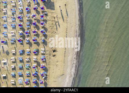 Luftblick auf den Sandstrand mit bunten Sonnenschirmen, Leute, die in der Bucht mit transparentem blauem Wasser an sonnigen Tagen im Sommer spazieren gehen. Larnaca, Cyprus Trav Stockfoto