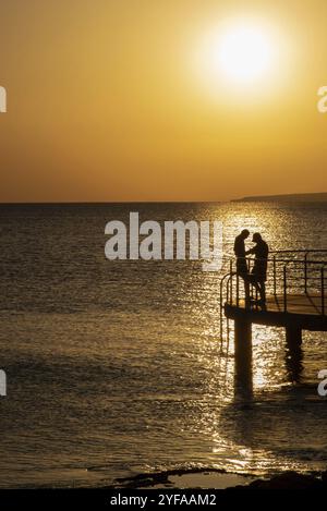 Silhouette eines jungen Paares, das den wunderschönen Sonnenuntergang am Strand genießt. Romantischer Moment, menschliche Beziehung am Ufer Stockfoto