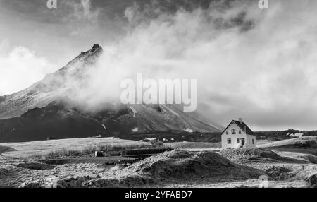 Schwarz-weiß-Bild einer typischen isländischen Winterlandschaft mit einem weißen kleinen schönen Haus unter dem Berg im Fischerdorf Arnarstapi snae Stockfoto