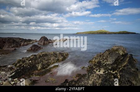 Felsküste aus Bellycotton mit Leuchtturm für die Meeressicherheit in Irland. Longexposure bewölkter Himmel Stockfoto