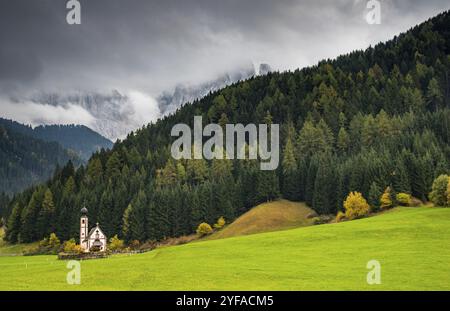 Die kleine und wunderschöne Kirche Saint John, Ranui, Chiesetta di san giovanni in Ranui Runes Südtirol Italien, umgeben von grüner Wiese, Wald an Stockfoto