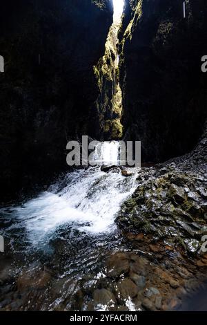 Majestätischer Wasserfall, der durch einen engen, moosbedeckten Canyon mit einem ruhigen Pool fällt Stockfoto
