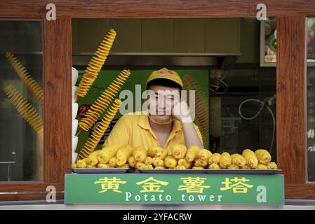 Peking, China ? 6. Juni 2018: Chefkoch in gelber Uniform, der traditionelle chinesische Gerichte auf einem Straßenmarkt in Peking in China verkauft Stockfoto