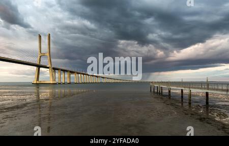 Vasco da Gama Brücke bei Sonnenuntergang mit dramatischem, bewölktem blauen Himmel in Lissabon, Portugal, Europa Stockfoto