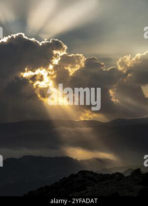 Helle Sonnenstrahlen leuchten bei Sonnenuntergang durch dunkle Wolken über dem Berg. Dramatischer Himmel im Winter Stockfoto