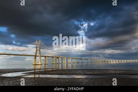 Vasco da Gama Brücke bei Sonnenuntergang mit dramatischem, bewölktem blauen Himmel in Lissabon, Portugal, Europa Stockfoto