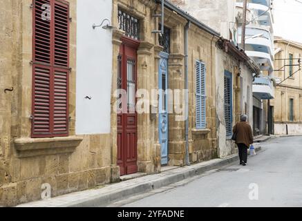 Unerkannte Seniorin mit einer Tasche Lebensmittel, die in einem Viertel mit alten traditionellen Häusern in den Straßen der alten Stadt Nikosia in Cypru spaziert Stockfoto