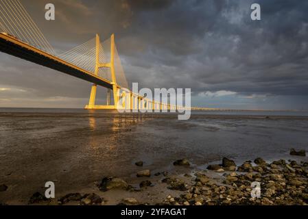 Vasco da Gama Brücke bei Sonnenuntergang mit dramatischem, bewölktem blauen Himmel in Lissabon, Portugal, Europa Stockfoto