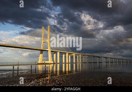 Vasco da Gama Brücke bei Sonnenuntergang mit dramatischem, bewölktem blauen Himmel in Lissabon, Portugal, Europa Stockfoto