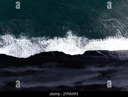 Aus der Vogelperspektive von Wellen, die an einem schwarzen Sandstrand in Island zusammenbrechen. Stockfoto