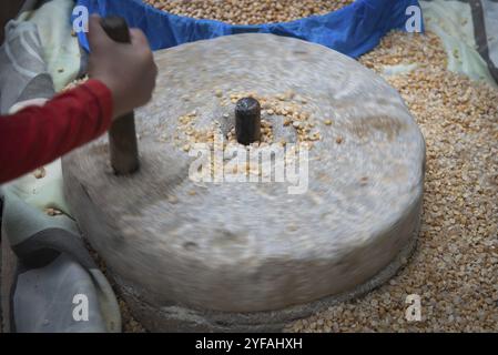 Menschliche Hand rotieren eine alte Steinschleifmaschine zum Zerschlagen von Körnern. Handgemachte manuelle Ausrüstung Mahlmühle Stockfoto