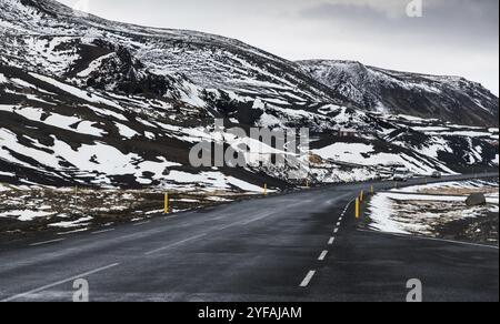 Ländliche leere gerade Straße auf der Halbinsel reykjanes in Island mit Richtung zu den teilweise schneebedeckten Bergen Stockfoto