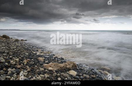 Meereswellen plätschern vor stürmischem, dramatisch bewölktem Himmel an die Küste mit Kieselsteinen. Winterzeit, Langlebigkeit Limassol zypern Stockfoto