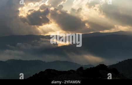 Helle Sonnenstrahlen leuchten bei Sonnenuntergang durch dunkle Wolken über dem Berg. Dramatischer Himmel im Winter Stockfoto