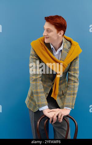 Ein junger Mann mit auffälligen roten Haaren posiert selbstbewusst in einem mehrlagigen Winteroutfit mit modischer Eleganz. Stockfoto