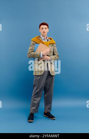 Ein junger Mann mit auffälligen roten Haaren steht selbstbewusst in einem stilvollen Winteroutfit und hält dabei eine Mappe in der Hand. Stockfoto