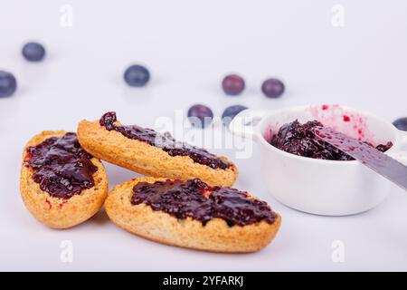 Toast mit Heidelbeermarmelade bedeckt und ein Glas daneben auf weißem Hintergrund. Ein einfacher, einladender Frühstücksmoment mit reichhaltigem Detail Stockfoto