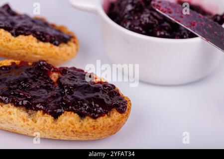 Toast mit Heidelbeermarmelade neben einem Glas auf weißem Hintergrund. Die Detailansicht verleiht dieser Frühstücksszene Farbe Stockfoto