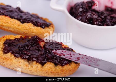 Toast mit Heidelbeermarmelade und einem Glas auf weißer Oberfläche. Das Bild zeigt ein frisches, lebendiges Frühstück in Nahaufnahme Stockfoto