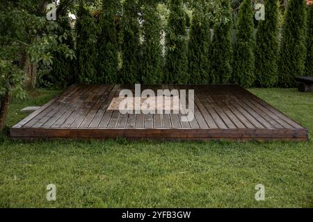 Holzterrasse mit zentralem Sandkasten im Hinterhof, umgeben von Bäumen und natürlicher Umgebung Stockfoto