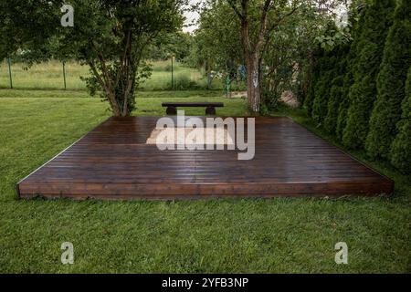 Holzterrasse mit zentralem Sandkasten im Hinterhof, umgeben von Bäumen und natürlicher Umgebung Stockfoto