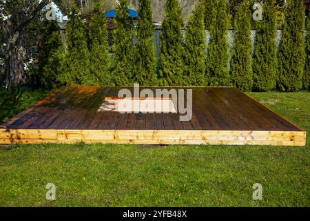 Frisch gebeizte Holzterrasse mit einem zentralen Sandkasten in einem Hinterhof umgeben von Bäumen und Büschen Stockfoto