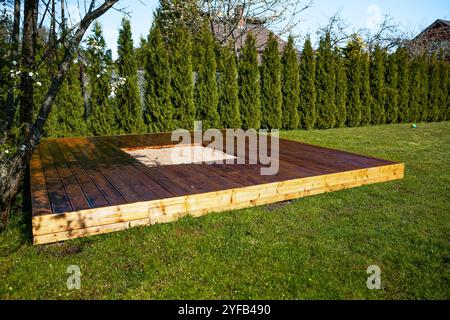 Frisch gebeizte Holzterrasse mit einem zentralen Sandkasten in einem Hinterhof umgeben von Bäumen und Büschen Stockfoto