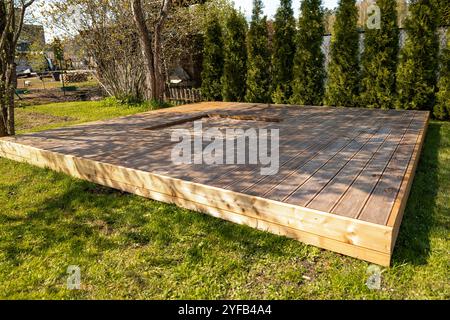 Holzterrasse mit zentralem Sandkasten im Hinterhof, umgeben von Bäumen und natürlicher Umgebung Stockfoto
