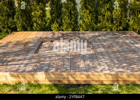 Holzterrasse mit zentralem Sandkasten im Hinterhof, umgeben von Bäumen und natürlicher Umgebung Stockfoto