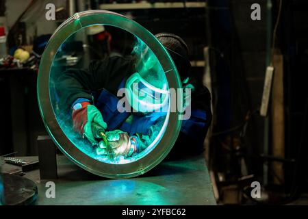 Schweißer arbeitet geschickt an einem großen Metallring, schweisst sorgfältig Verbindungen in einer gut ausgestatteten Werkstatt. Stockfoto