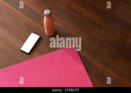 Yogamatte, Smartphone und Wasserflasche auf Holzboden für Heimtraining, Kopierraum Stockfoto