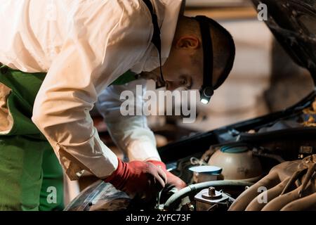 Mechaniker, der detaillierte Reparaturen unter der Motorhaube mit Scheinwerfer durchführt. Stockfoto