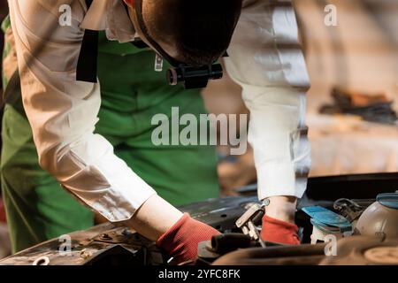 Mechaniker, der Wartungsarbeiten an einem Fahrzeug in einer schwach beleuchteten Werkstatt durchführt. Stockfoto