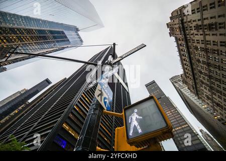 Ein dramatischer, flacher Blick auf die hoch aufragenden Wolkenkratzer in New York City mit einem Fußgängersignal im Vordergrund, das die urbane Atmosphäre einfängt Stockfoto