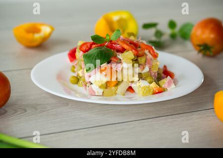 Gemüsesalat aus gekochtem Gemüse, mit Erbsen, Wurst, süßem Pfeffer. Auf einem Holztisch. Stockfoto