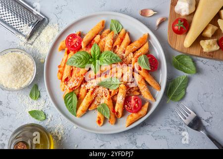 Klassische italienische Pasta Penne alla arrabiata mit Basilikum und frisch geriebenem Parmesankäse auf dunklem Tisch. Penne mit Chilisauce arrabbiata. Stockfoto