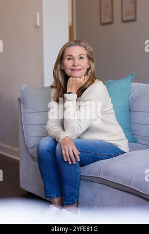 Lächelnde Seniorin sitzt zu Hause auf der Couch und genießt einen entspannten Nachmittag Stockfoto