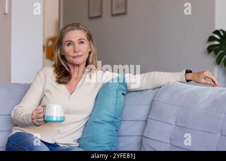 Entspannen Sie sich zu Hause, eine ältere Frau genießt Kaffee auf einem gemütlichen Sofa Stockfoto