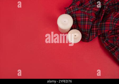 Gemütliche Kerzen und karierter Stoff auf rotem Hintergrund - minimalistisches Wärme- und Komfortkonzept für Innendesign und saisonale Einrichtung Stockfoto
