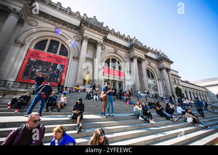 Die Menschen sitzen und entspannen sich auf den legendären Stufen des Metropolitan Museum of Art (The Met) in New York City mit der großen neoklassizistischen Fassade. Stockfoto