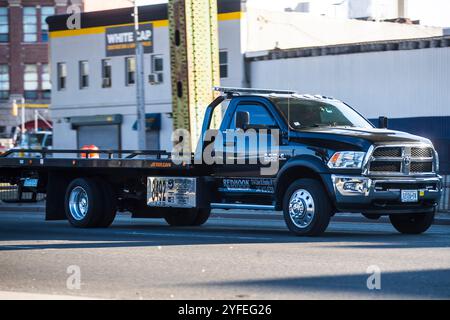 Schwarzer Abschleppwagen, der auf einer Stadtstraße in der Nähe von Industriegebäuden fährt. Stockfoto