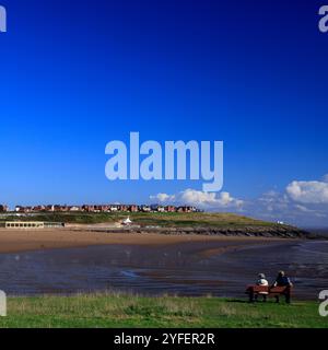 Älteres Ehepaar, das auf einer Bank sitzt und über Whitmore Bay, Barry Island, Vale of Glamorgan, Südwales, Großbritannien blickt. Oktober 2024 Stockfoto