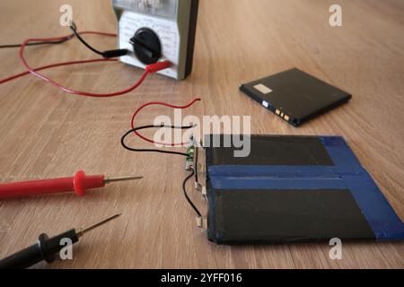 Lithium-Ionen-Batterien mit flacher Zelle auf dem Tisch. Batterieprüfung mit Voltmeter. Auf die Vorderseite ausgerichtet. Stockfoto