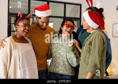 Mit festlichen Hüten und multirassischen Freunden lachen zu Hause während der Weihnachtsfeier zusammen Stockfoto