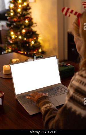 Ältere Frau, die zu Hause den Laptop benutzt, Weihnachtsbaum im Hintergrund glüht, Kopierraum Stockfoto